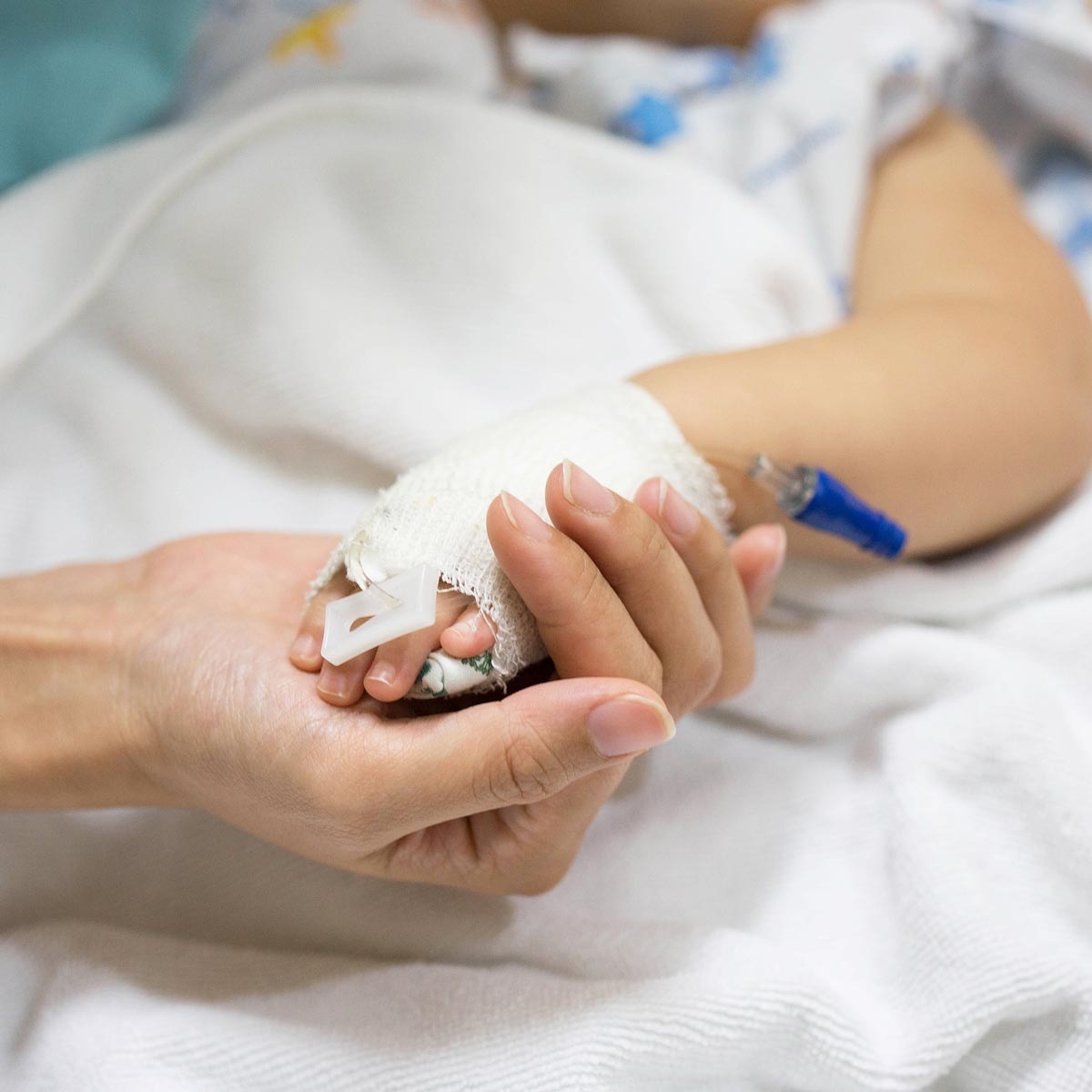 caregiver holding the bandaged hand of a child in a hospital bed